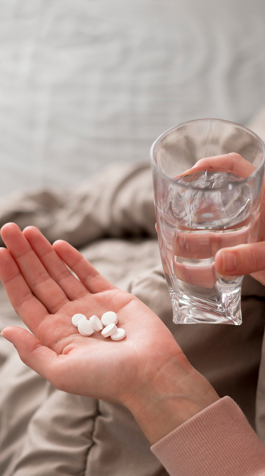 A person holding white pills in one hand and a glass of water in the other.