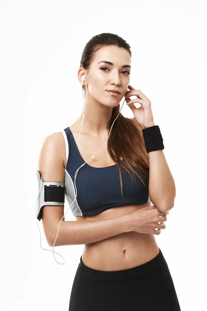 A woman in sportswear listening to music with headphones, looking confidently at the camera.